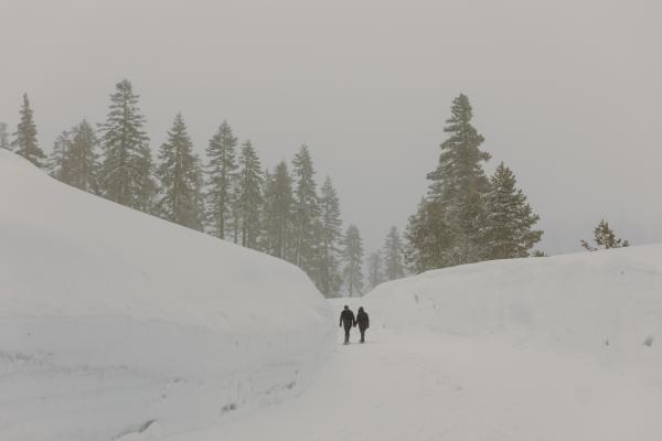couple walking down a snow covered road with a tall snow burm on both sides